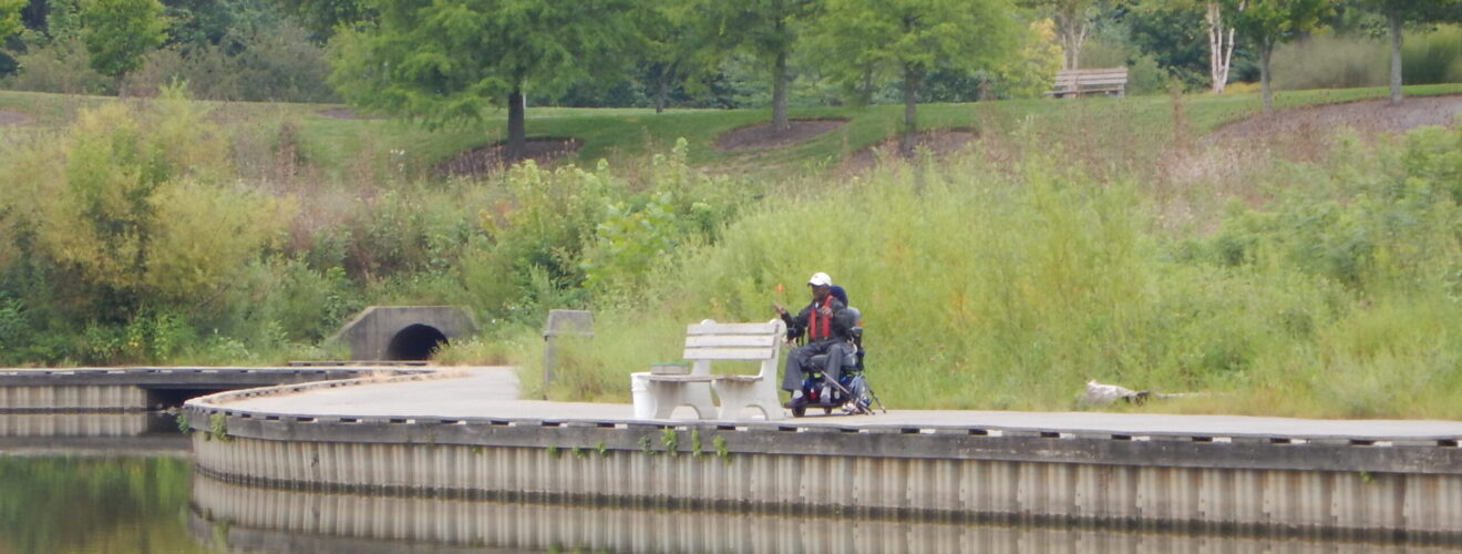 Man seated in wheelchair fishing along the lake.