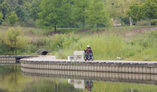 Man seated in wheelchair fishing along the lake.